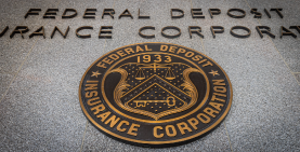 image of the FDIC seal on the exterior marble wall of the FDIC main building looking up at angle from below with Federal Deposit Insurance Corporation above it